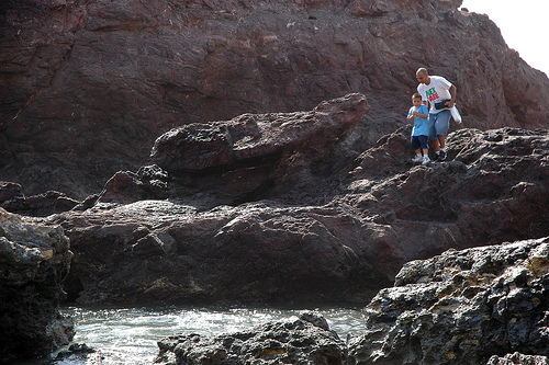 A man encouraging his son to walk on rocks, Mex Sabe t-shirt, carrying a tackle box, South Mazatlan, Mexico